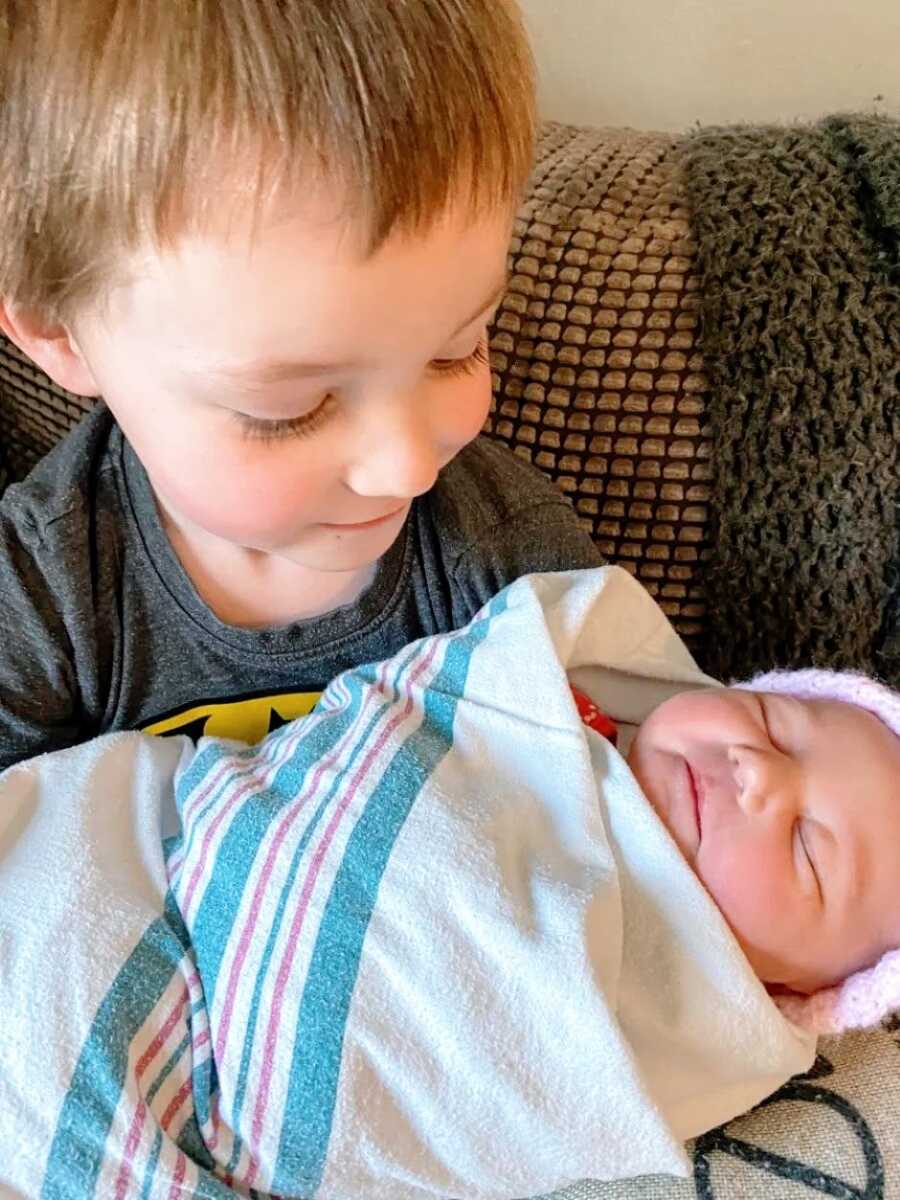 Big brother holds his newborn baby sister on the couch while she sleeps