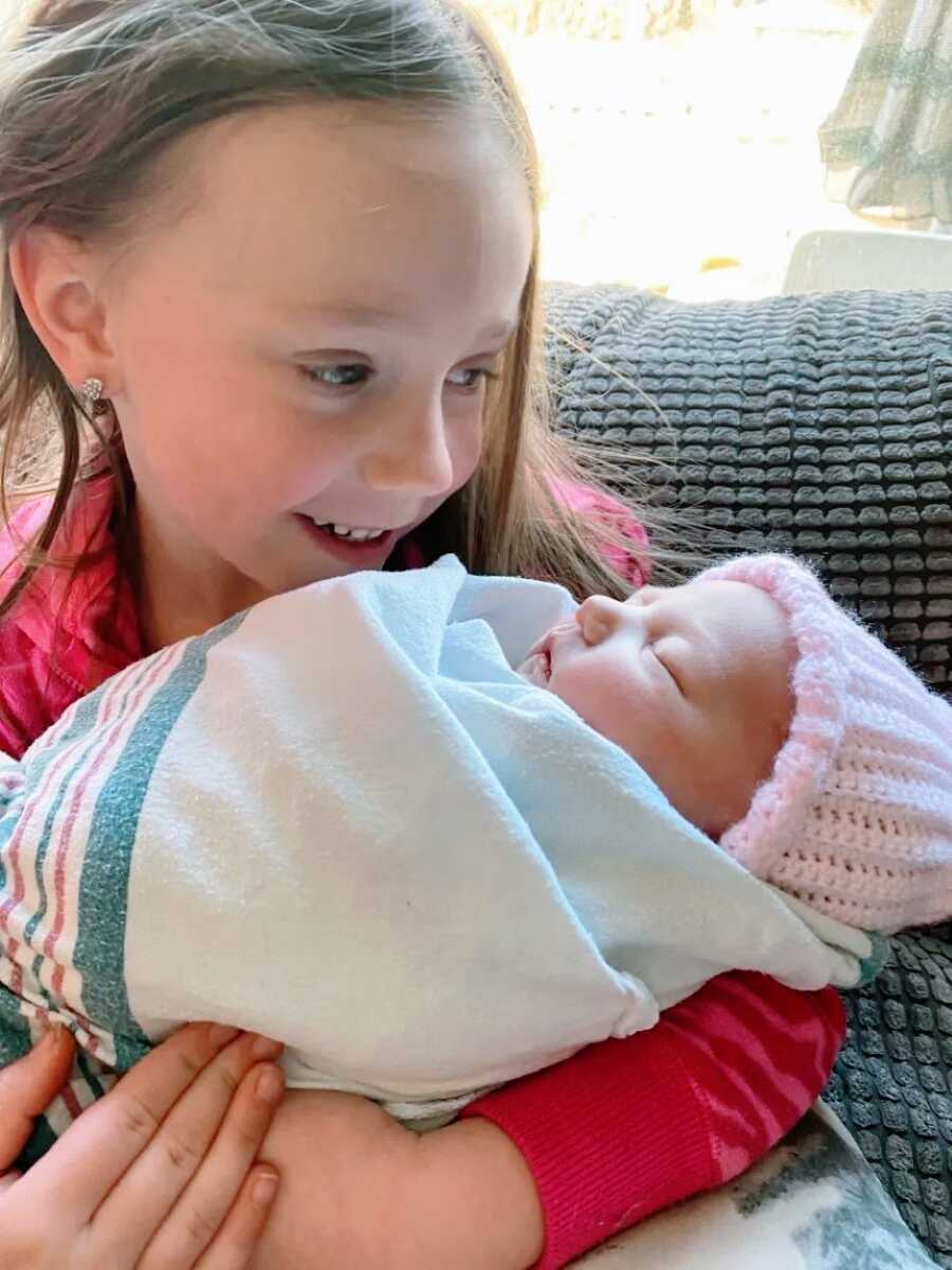 Big sister holds her newborn baby sister while sitting on the couch