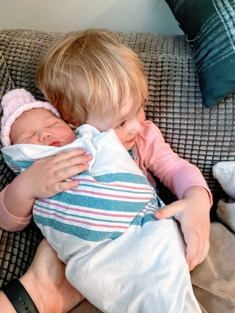 Little girl hugs her newborn little sister while sitting on the couch