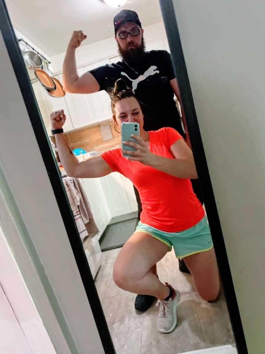 Couple take mirror selfie together while flexing in workout clothes