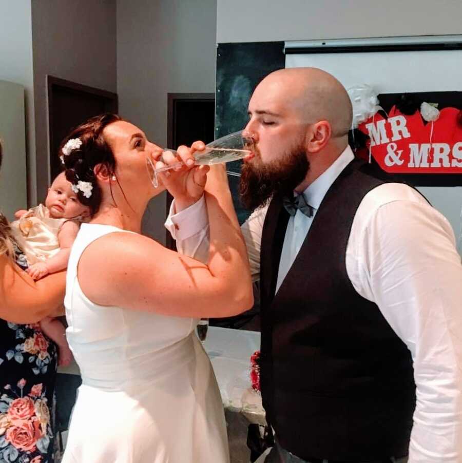 Newlyweds interlink their arms and drink a glass of champagne at their wedding