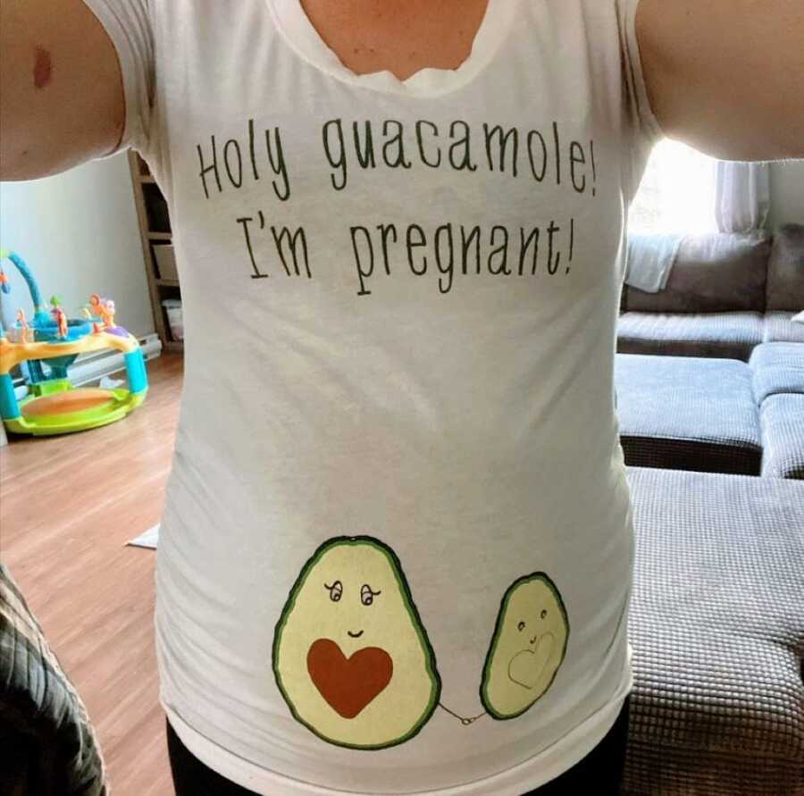 Woman takes a photo of her belly bump while wearing a shirt that reads "Holy guacamole! I'm pregnant!"