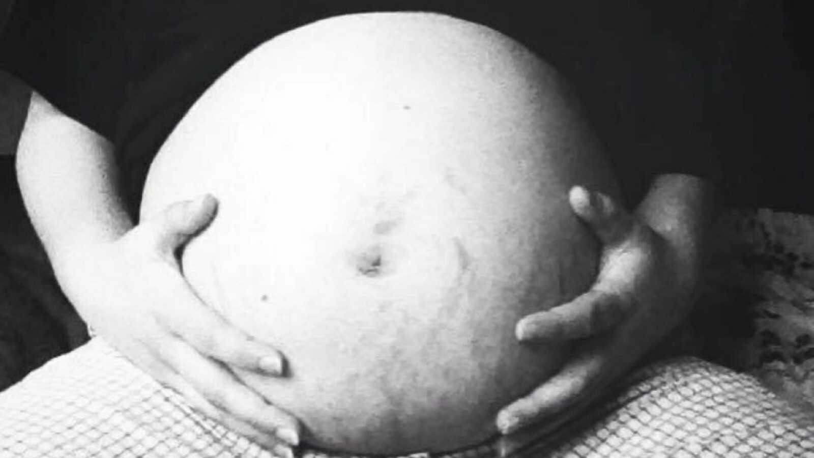 Very pregnant woman takes a close up of her growing belly while she holds it