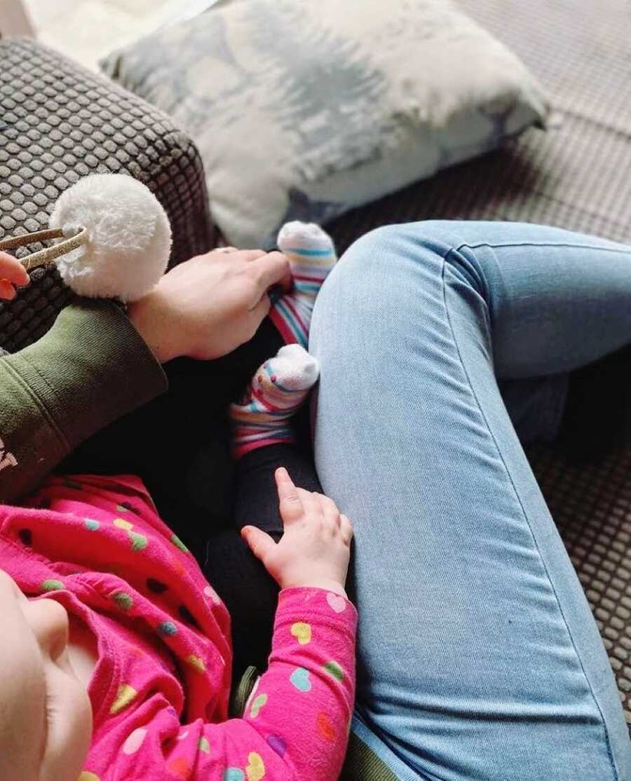 Mom snuggles with her young daughter on the couch while she plays with a toy 