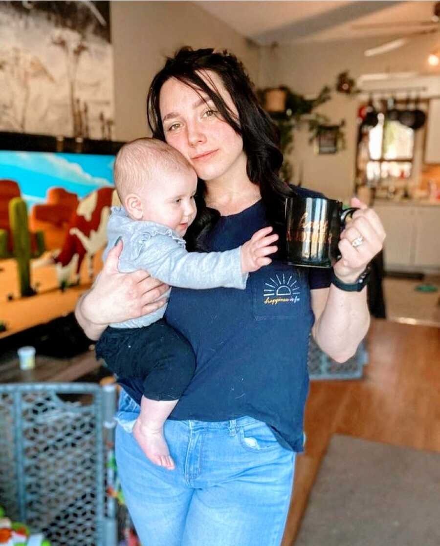Mom rests her cheek on her baby's head while her baby tries to steal her cup of coffee