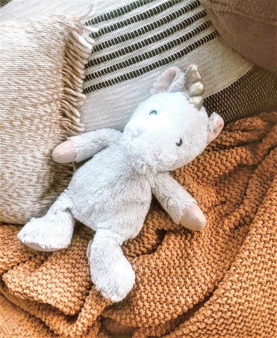 white stuffed unicorn laying on top of a blanket in the couch 