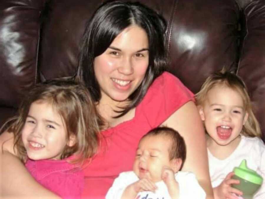 Asian American mom sitting on the couch with her three kids - one baby and two toddler girls