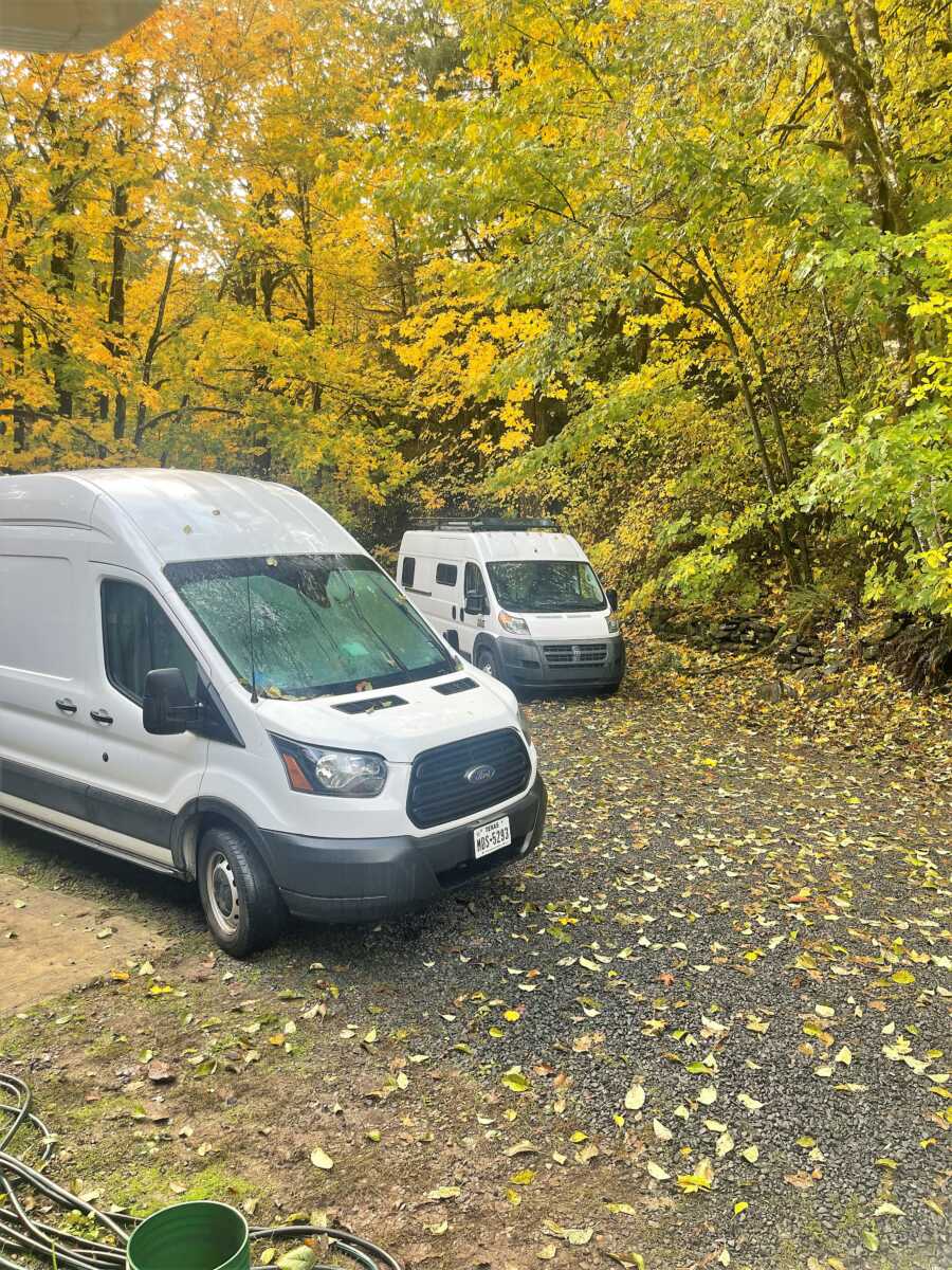 two white camper vans parked at a campsite during a fall day with yellow trees around