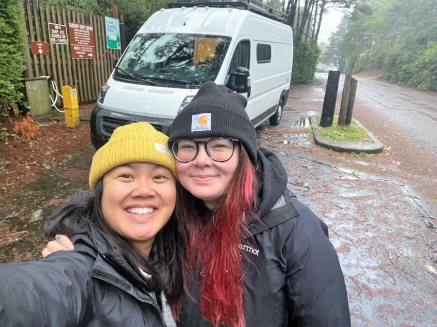 selfie of LGBT couple smiling standing in front of their white camper van 