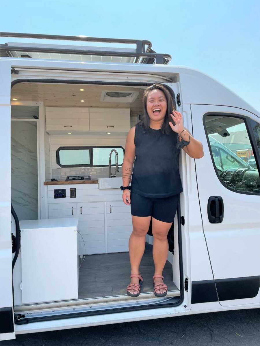 Girl standing at the entrance of a white camper van and smiling