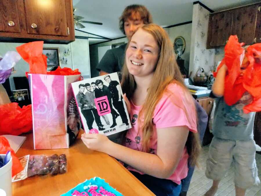 Teen girl holds up a One Direction at her birthday party and smiles