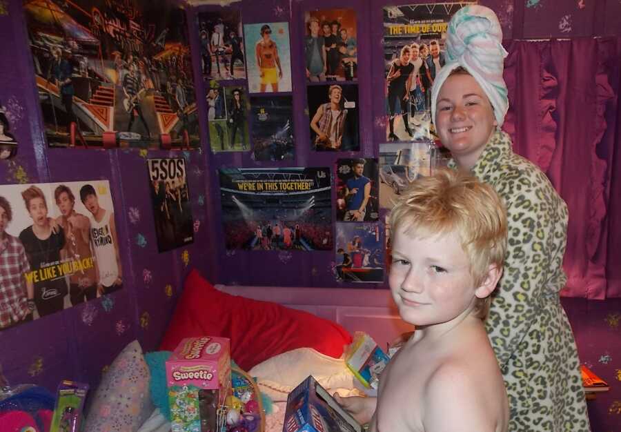 Siblings smile for a photo while opening their Easter baskets with the daughter's posters in the background