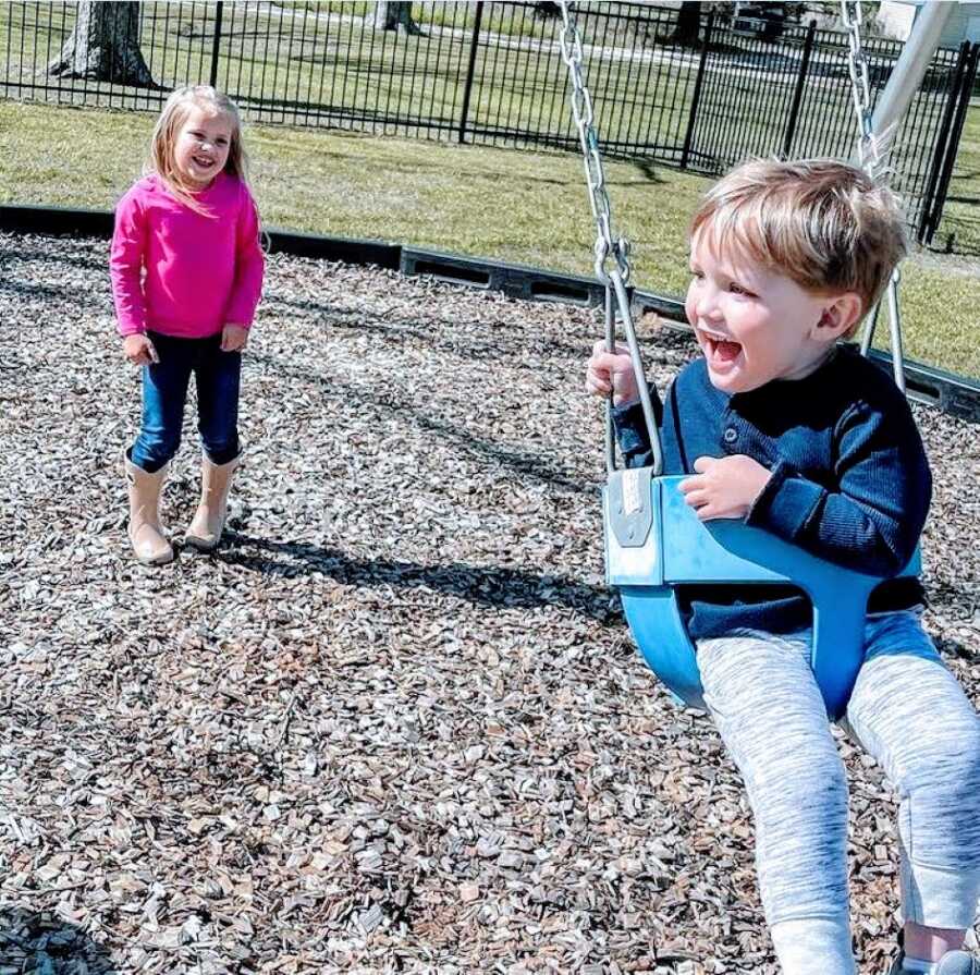 Big sister pushes her little brother with autism on a swing at the park