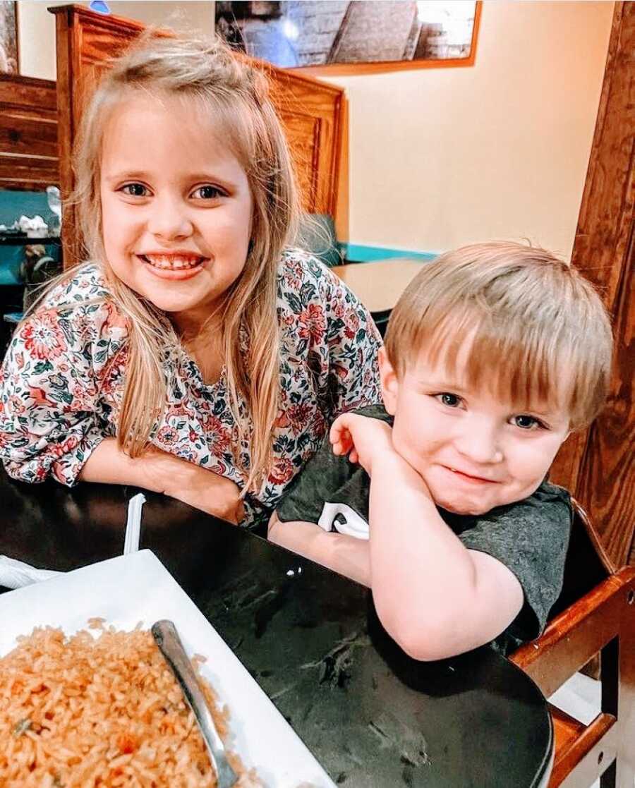 Brother and sister smile for a photo together while out for lunch at a restaurant with their family