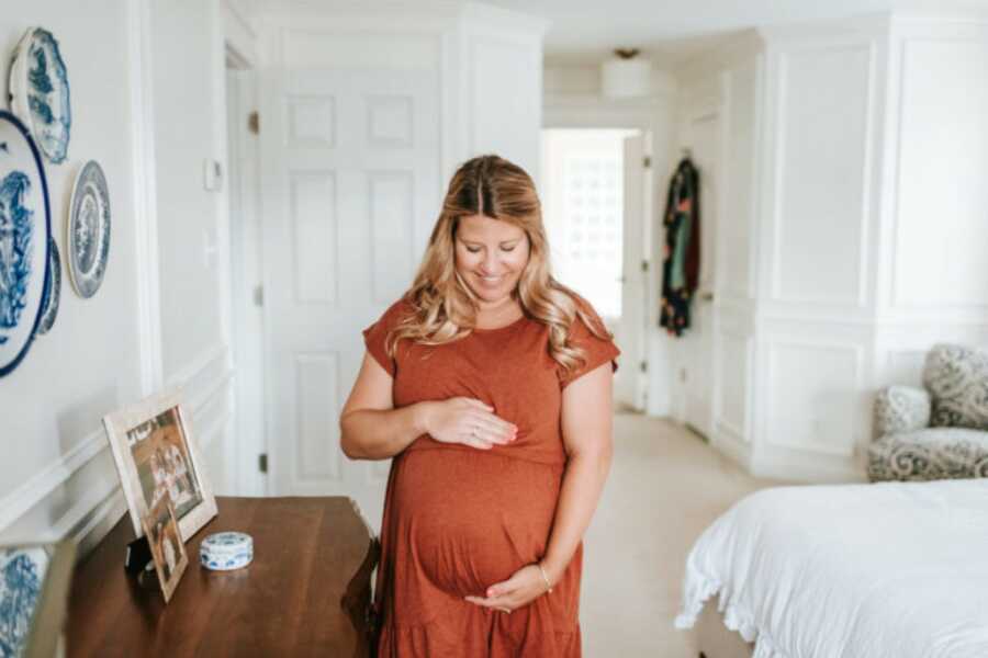 Pregnant woman in an orange dress cradling her belly