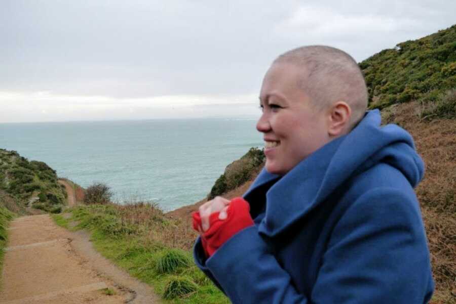 Woman battling cancer smiles while on a hike with the ocean behind her