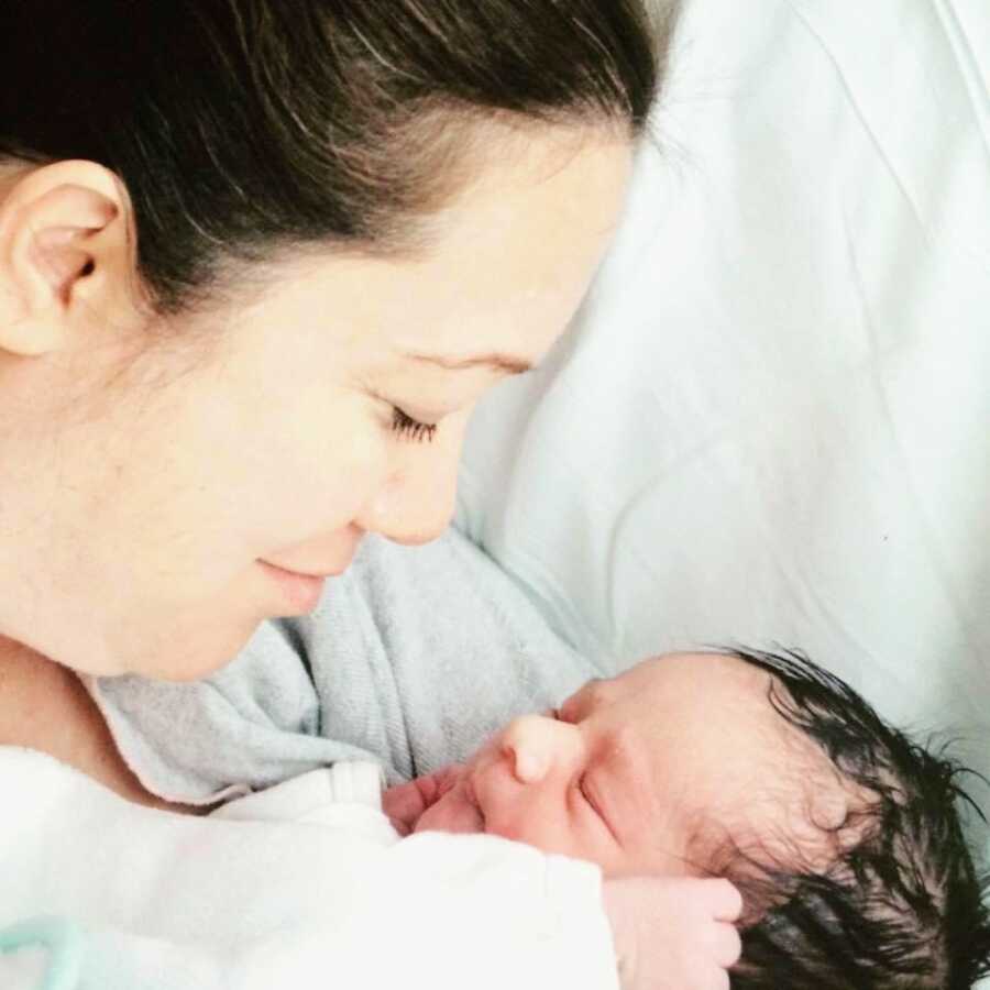 New mom smiles down at her newborn daughter sleeping in her arms