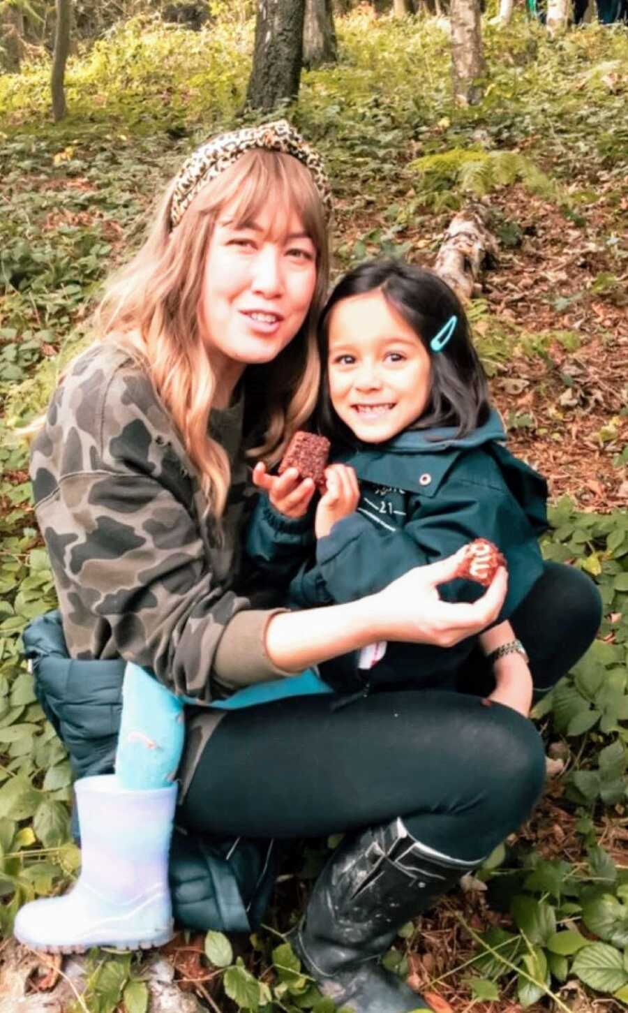 Mom and daughter take a break on a hike to eat a snack together in the woods