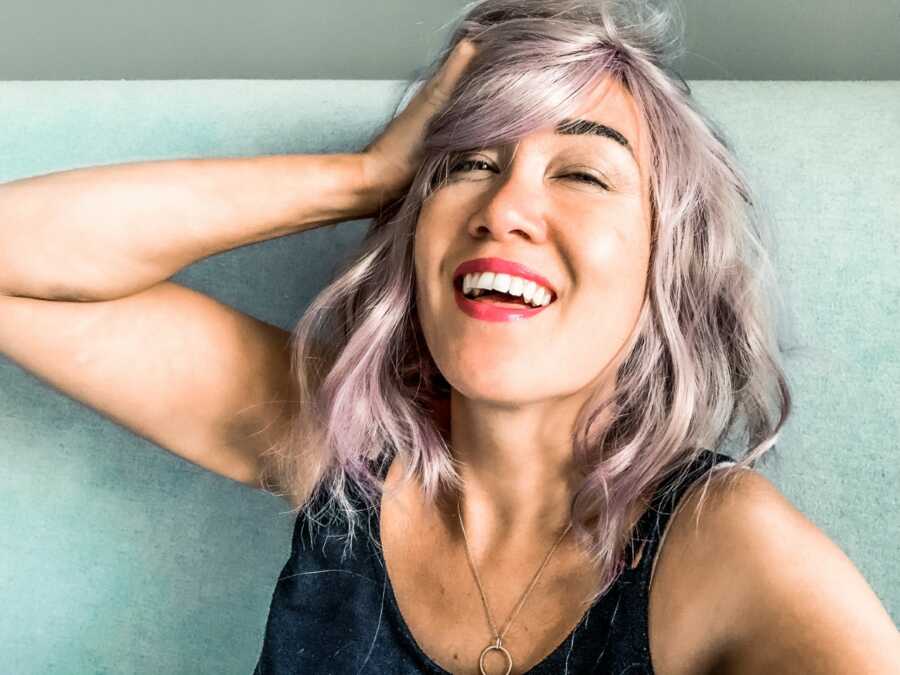Woman learning self care takes a selfie while wearing a purple wig