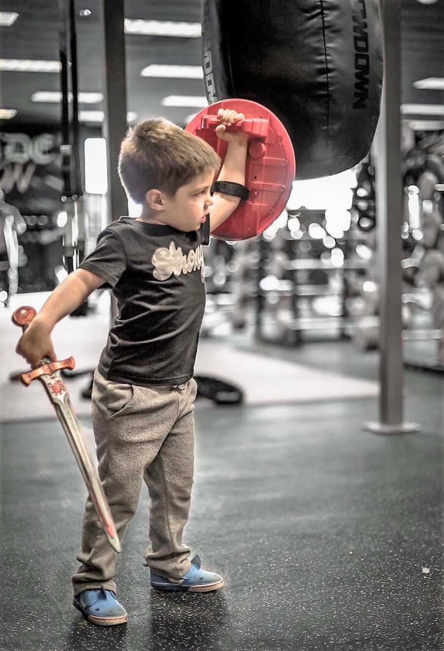 Toddler boy playing with sword and shield toys at the gym