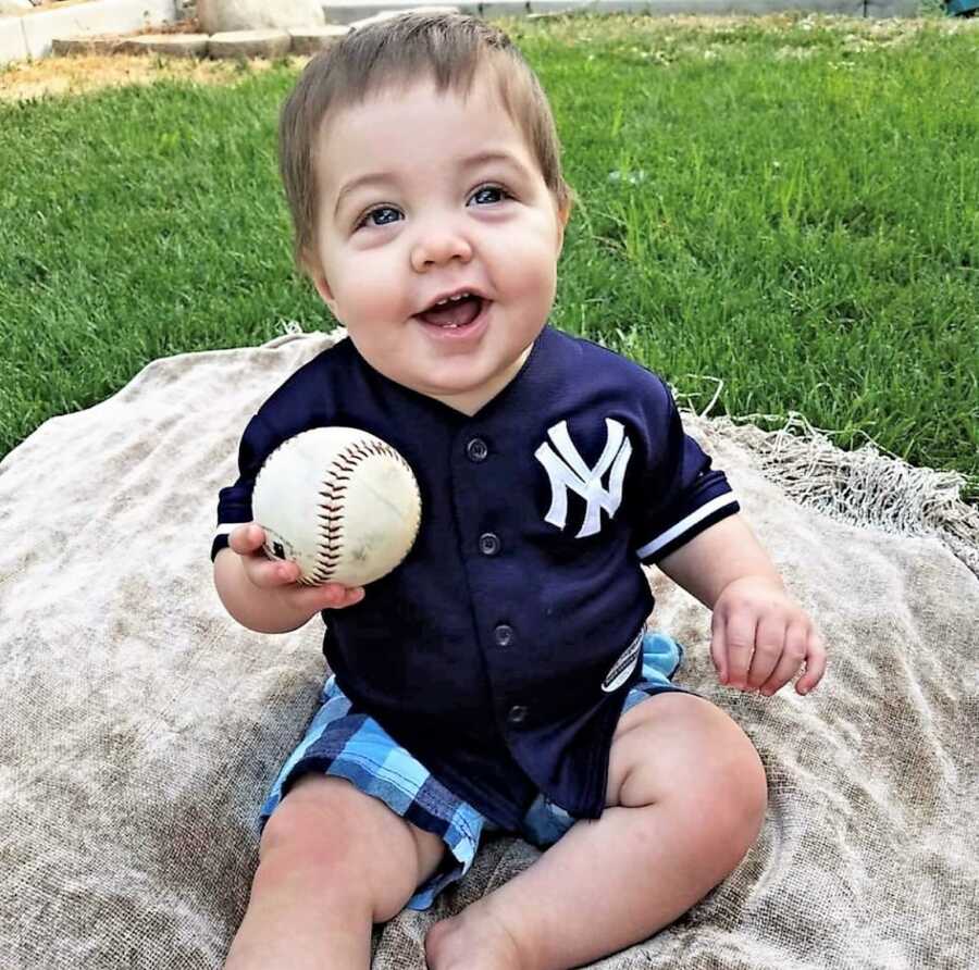 baby boy wearing a Yankee's shirt and holding a baseball ball