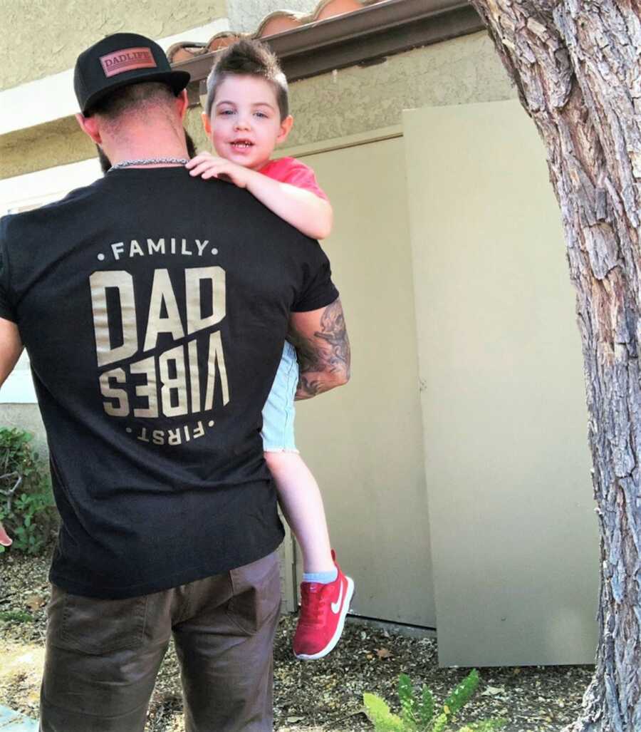 picture of the back of a dad carrying his toddler son and wearing a shirt that says "DAD VIBES"
