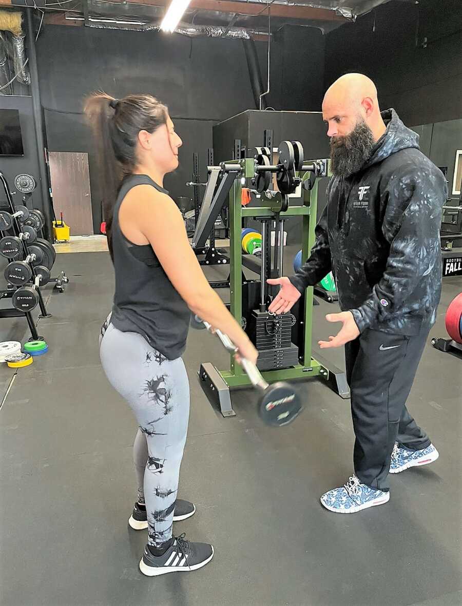Personal trainer guiding a female client holding a barbell at the gym