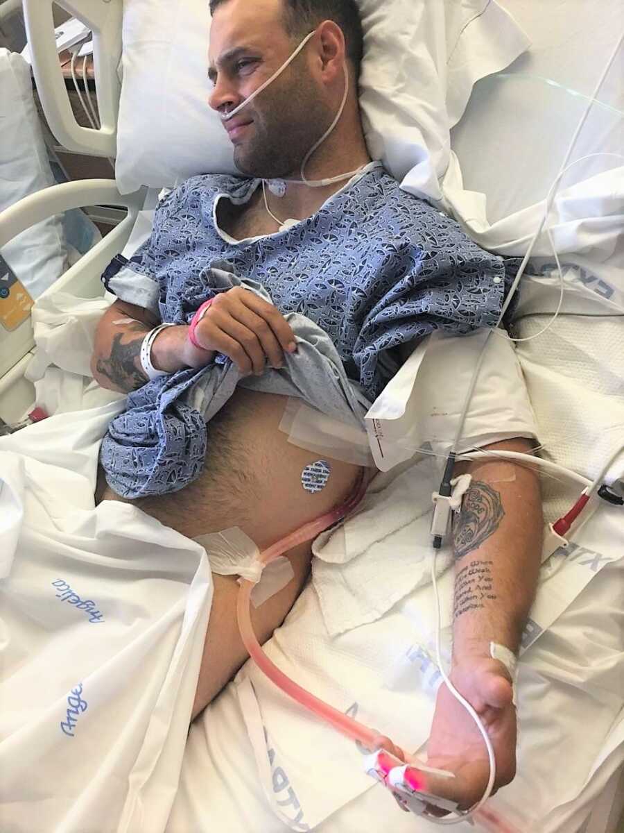 man laying in a hospital bed with IV fluids attached to his body and oxygen concentrator 