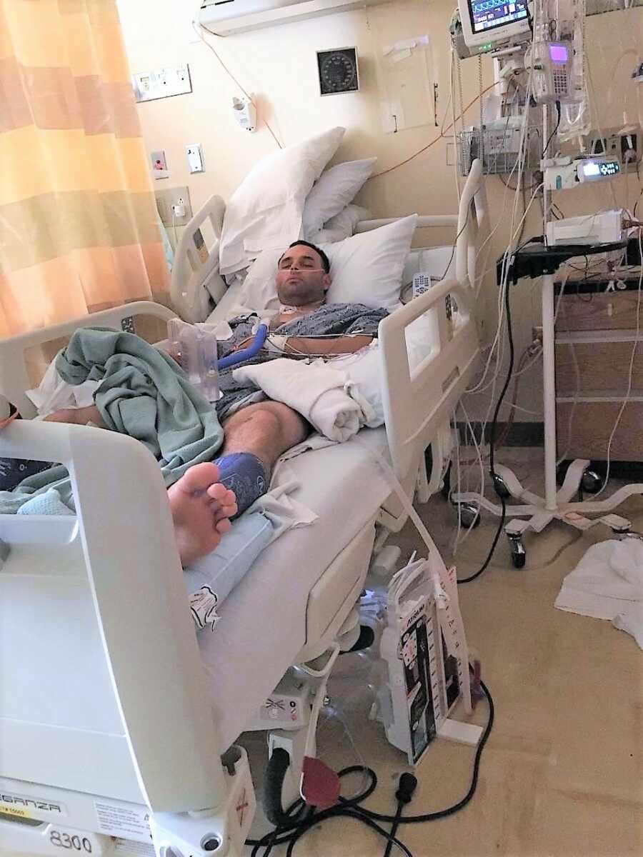 man laying in a hospital bed with IV fluids attached to his body and oxygen concentrator 