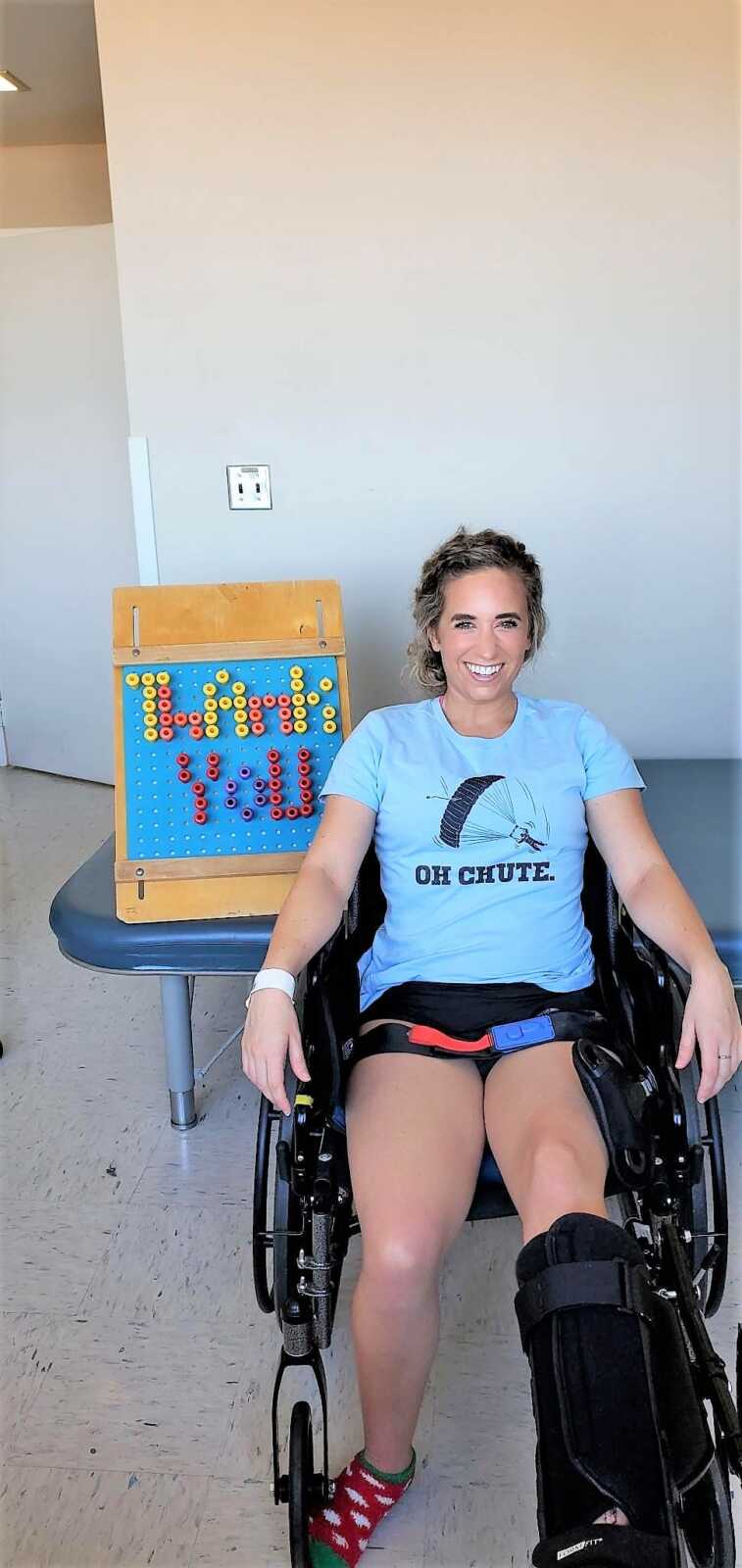 Young woman sitting in a wheelchair with a char that says "OH CHUTE" and a sign that says "THANK YOU"