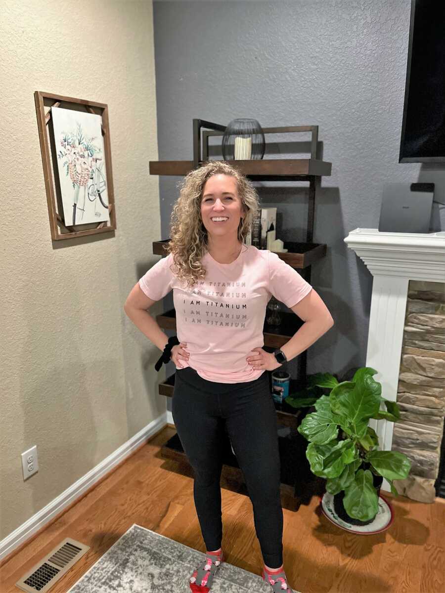 Woman who just recovered from skydiving accident standing up with her hand on her waist and wearing a shirt that says "I AM TITANIUM" 
