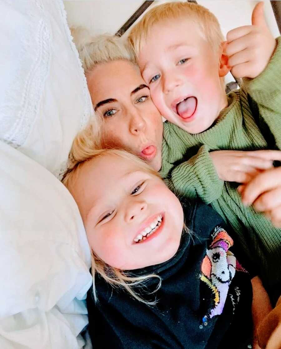 Mom takes a selfie with her two children while they cuddle together in bed