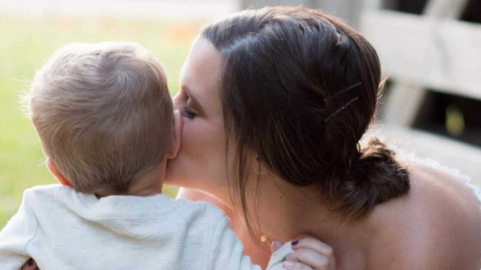Mom of two kisses her firstborn son on the cheek during a family photoshoot