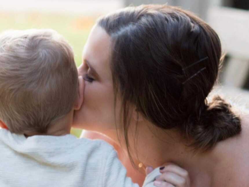 Mom of two kisses her firstborn son on the cheek during a family photoshoot