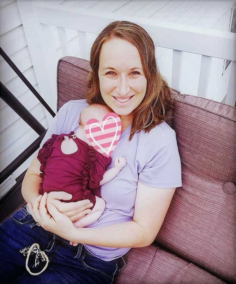 Gestational carrier holding newborn baby girl while laying on a couch 