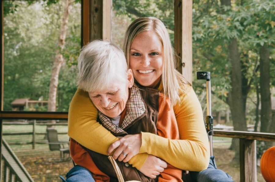 Woman in yellow long-sleeved shirt hugs her mom from behind
