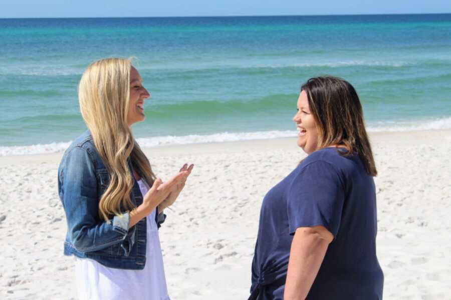 Two foster moms take candid photo on the beach while they talk and laugh with one another