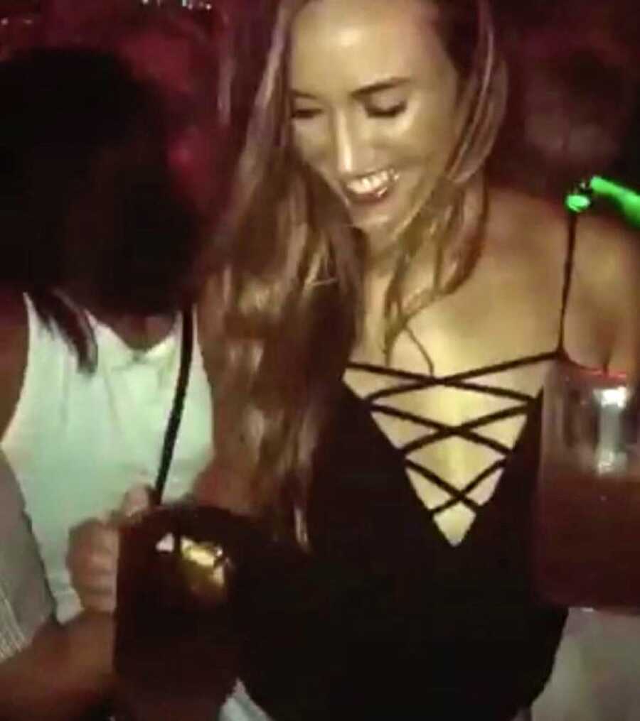 Young woman holds two drinks in a club while wearing a low-cut black tank top
