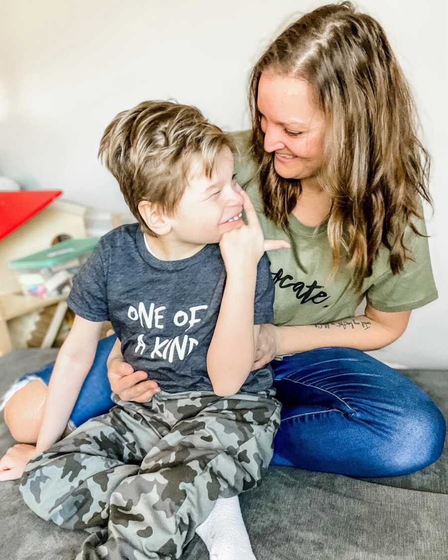 Mom smiles down at her son born with a rare disease while she holds him in her lap