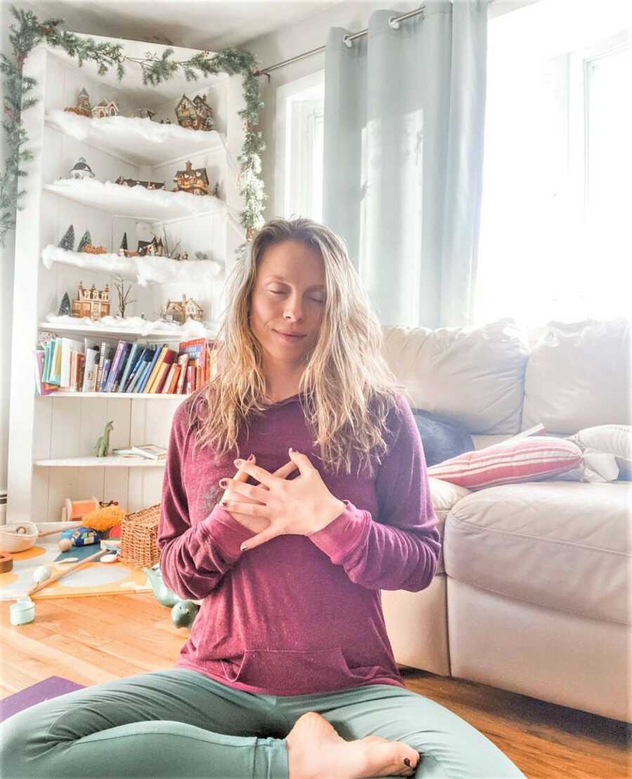 Woman meditating on the floor with her legs crossed and her hand on her chest 