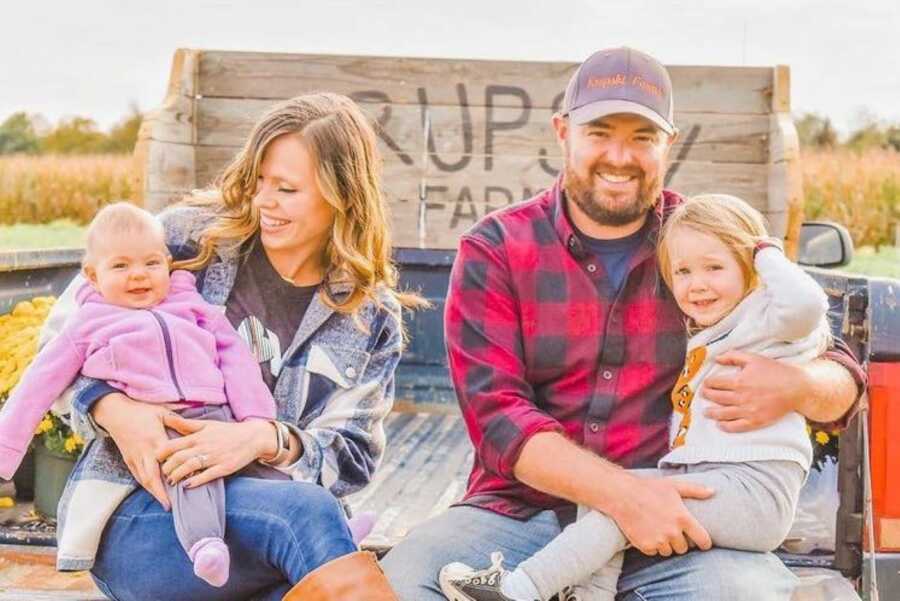 Family of four take fall-themed photos during golden hour while sitting in the back of a truck