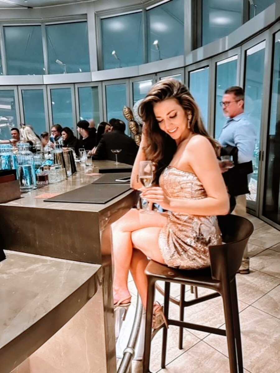 Woman wears fancy, sparkly cocktail dress while mussing her hair and holding a glass of champagne
