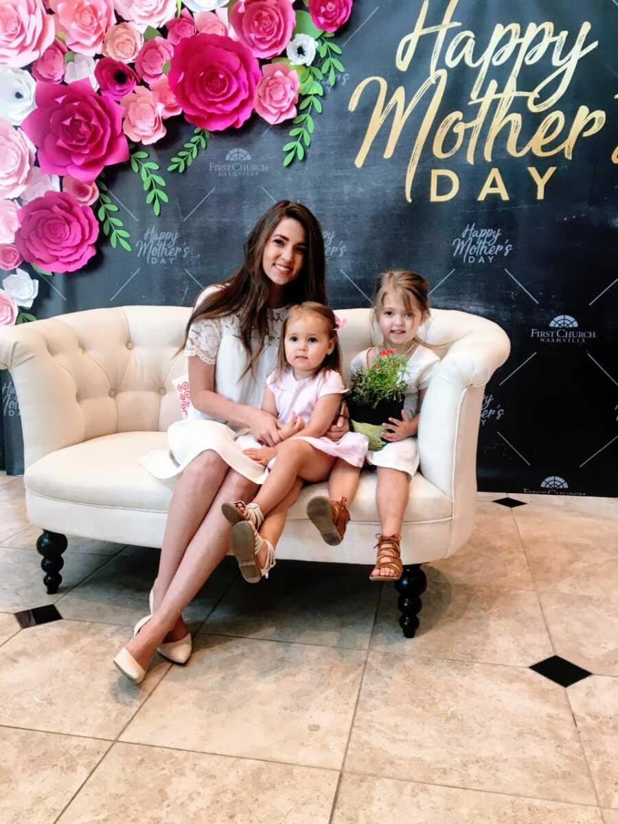 Woman takes a photo with her two daughters while sitting on a white couch at a Mother's Day banquet