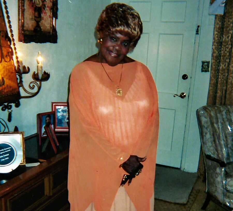 African American woman smiles for a photo in her living room while wearing an orange and white outfit