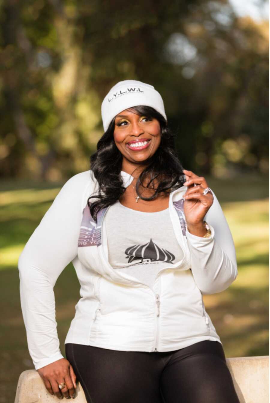 African American woman wearing matching white outfit with the logo and initials of her company called Living Your Life Without Limits