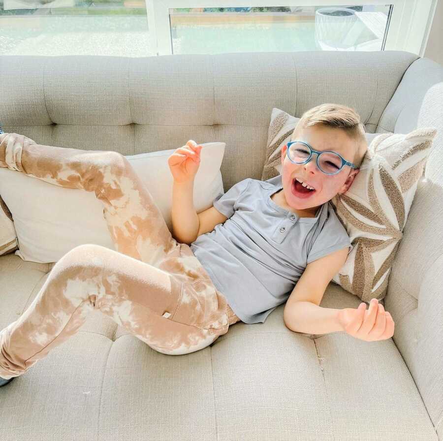 5-year-old boy with Sturge-Weber Syndrome laying in the couch laughing with his legs extended in the air 