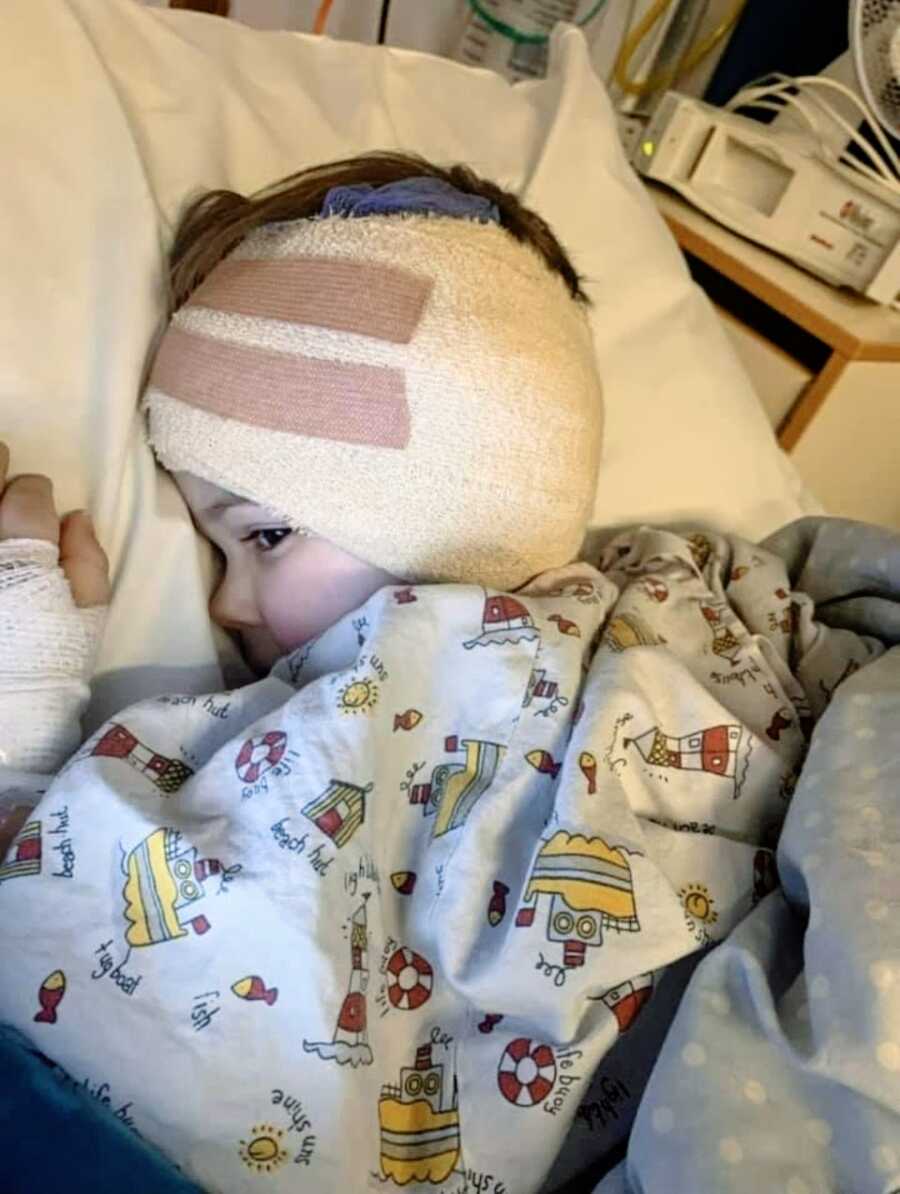 Little boy with rare hearing loss disorder lays in a hospital bed with bandages wrapped around his head