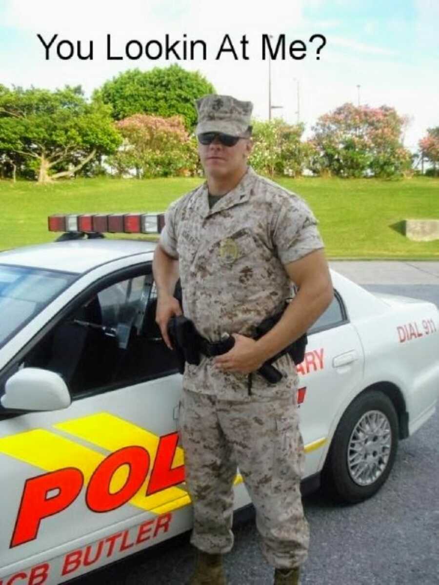 Marine serving in the military police takes a serious photo next to a police car
