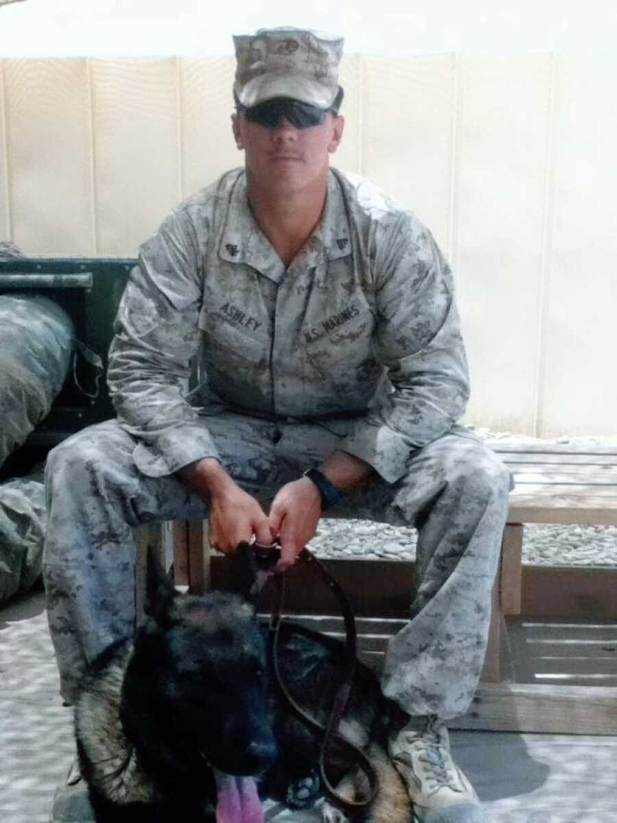Young Marine Corps sits on bench in Afghanistan while holding the leash of his K-9 partner
