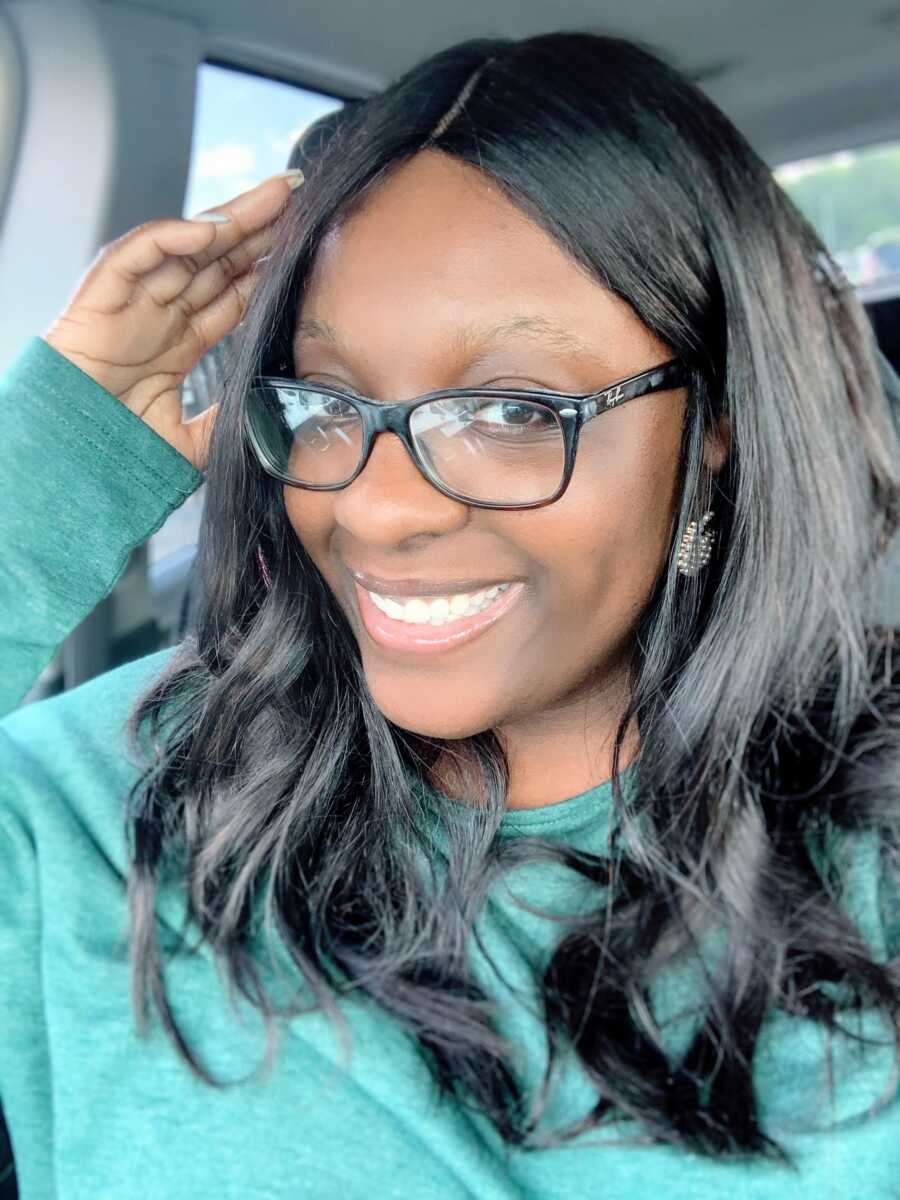 Woman takes selfie in the car while wearing black glasses and green long-sleeved shirt